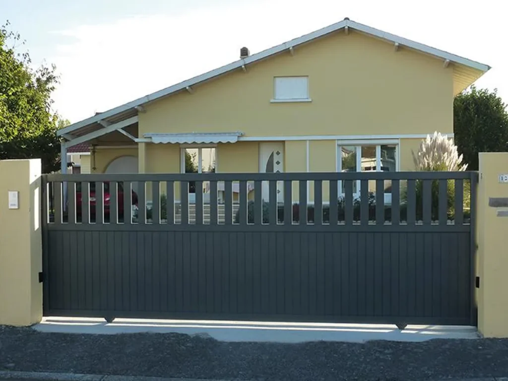 Portail coulissant aluminium gris à barreaudage vertical, refermé entre deux piliers maçonnés