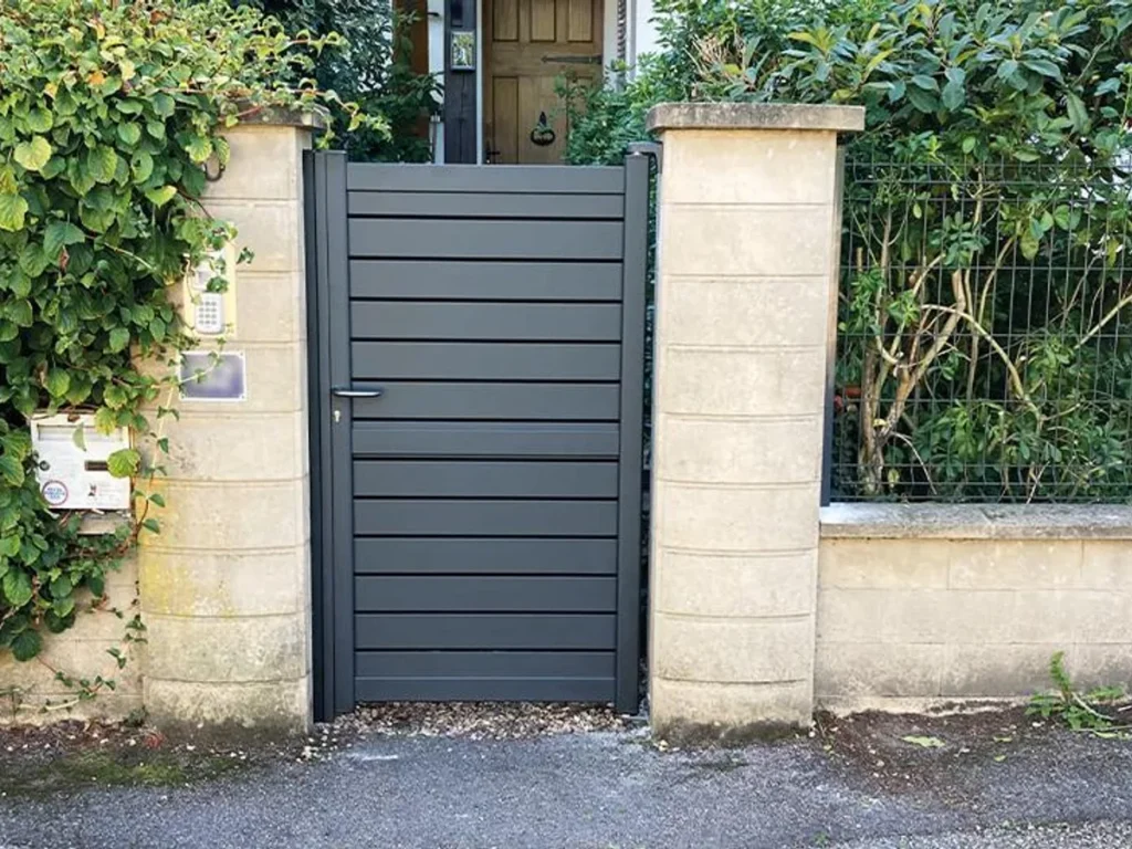Portillon aluminium gris à lames horizontales, assorti au portail, sur une entrée de maison