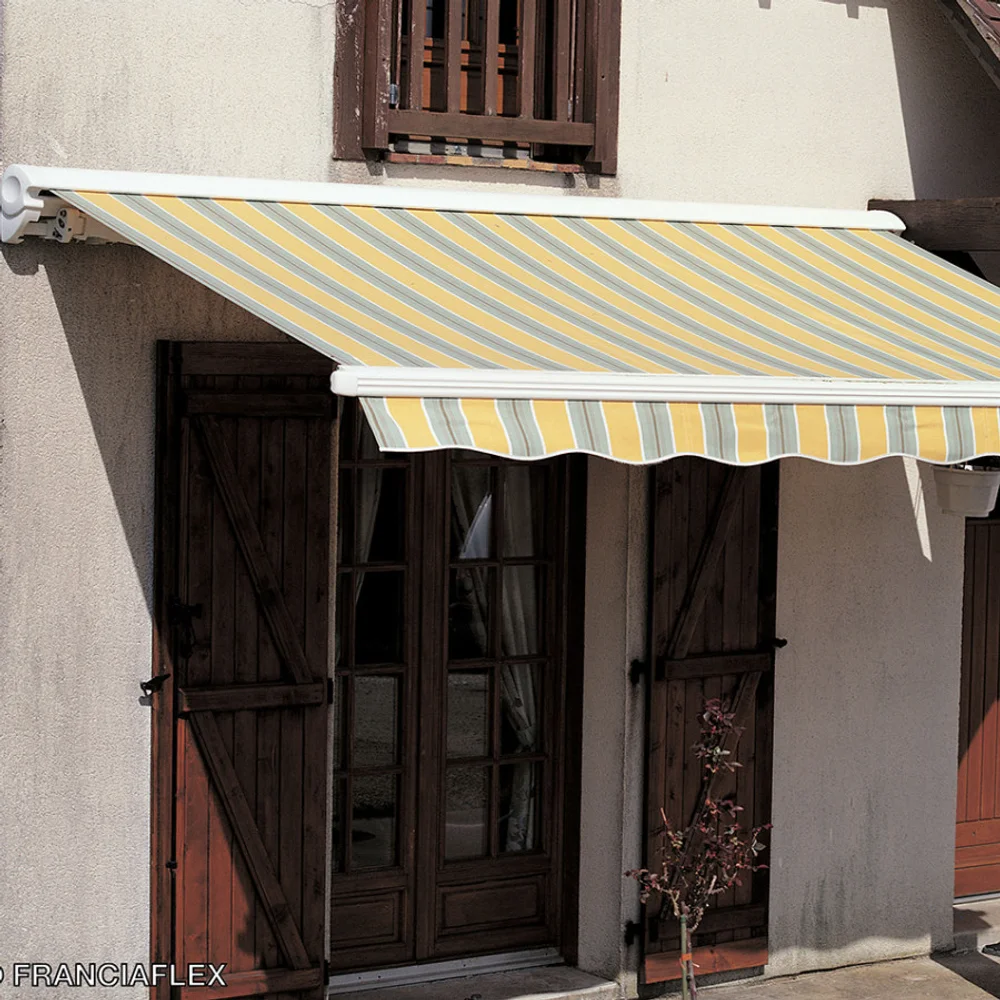 Store banne à toile rayée jaune et blanche sur une façade en pierre avec volets bois