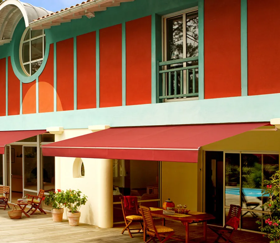 Stores extérieurs à toiles rouge et verte sur une façade colorée avec terrasse en bois