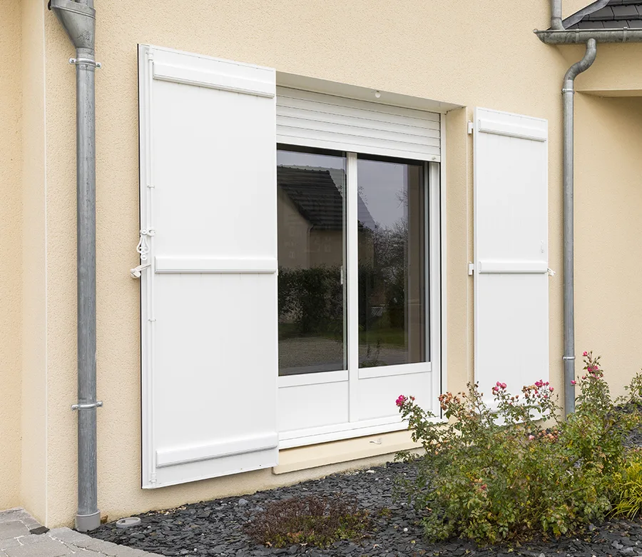 Volets battants aluminium blancs à lames persiennes encadrant une fenêtre