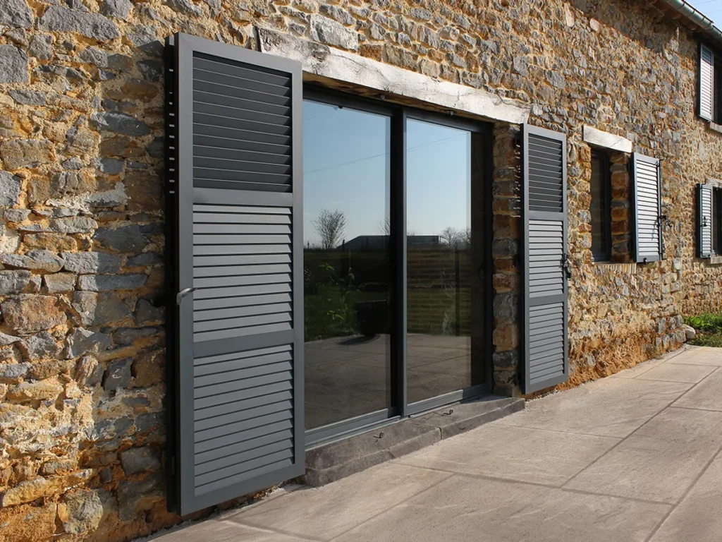 Volets battants aluminium gris anthracite à lames persiennes sur une maison en pierre