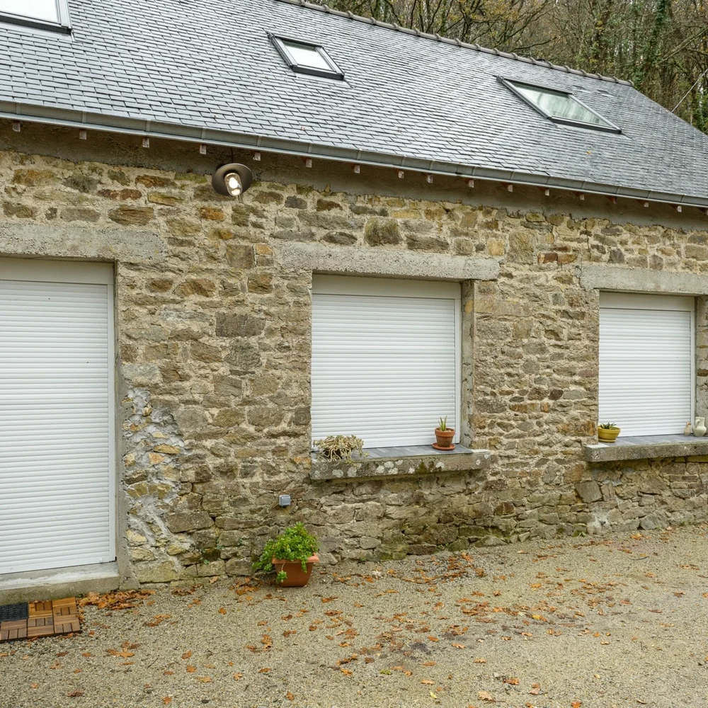 Volet roulant PVC blanc sur la fenêtre d’une longère en pierre