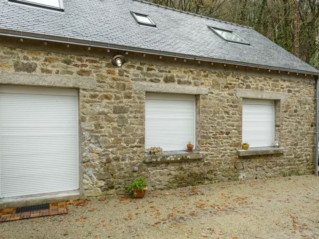 Volets roulants PVC blancs installés sur les fenêtres d’une maison en pierre